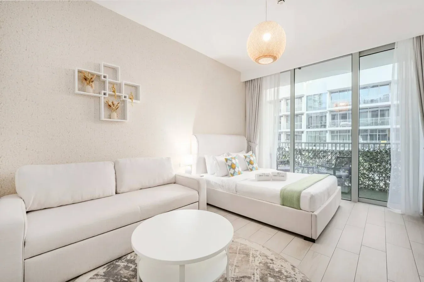 Un dormitorio luminoso con cama, asientos y grandes ventanales con salida a un balcón.