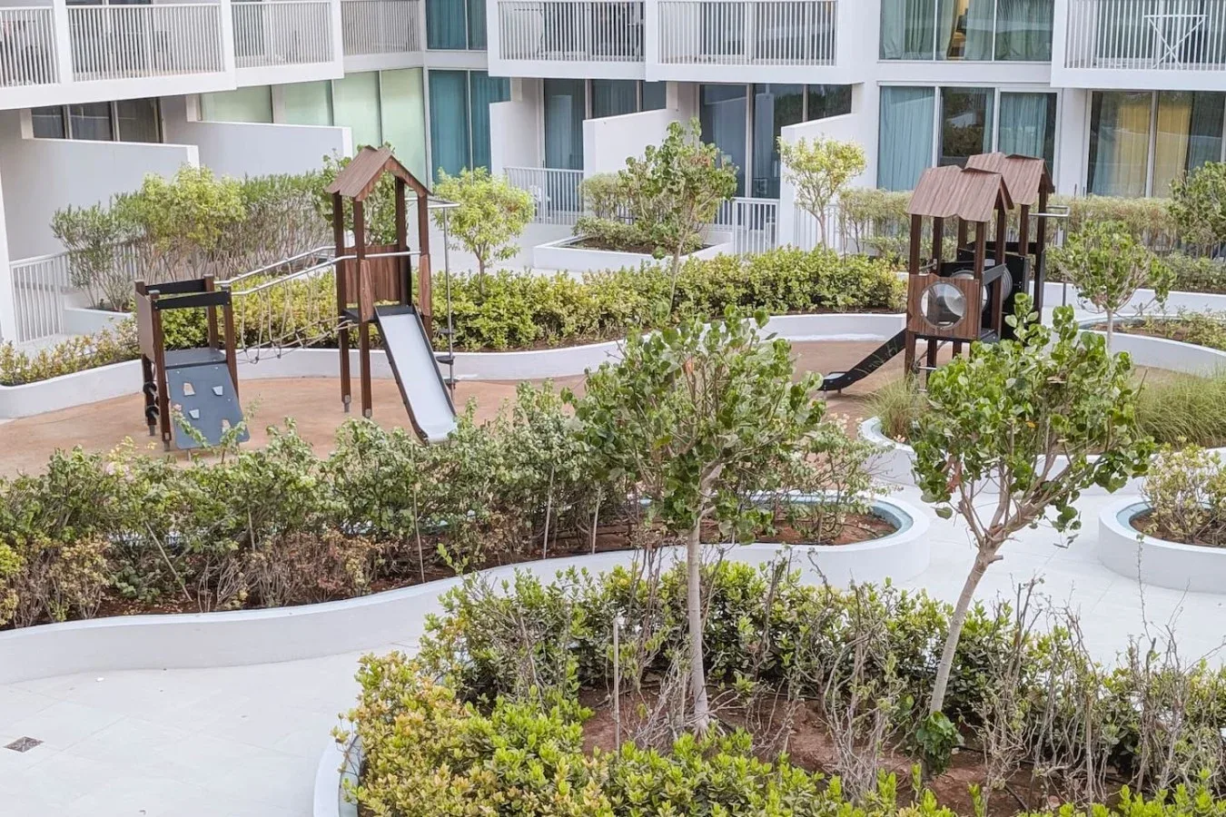Un parque infantil en un patio ajardinado, con toboganes, estructuras para trepar y vegetación.