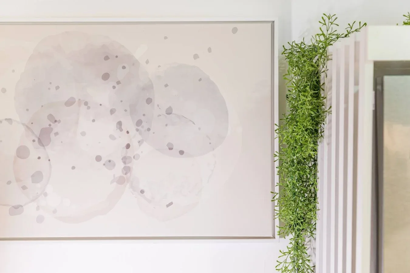 Una lámina abstracta enmarcada cuelga junto a una planta verde colgante.