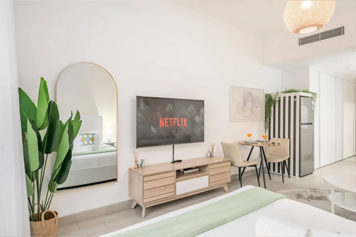 Una sala luminosa con televisor, mueble de madera y mesa de comedor.
