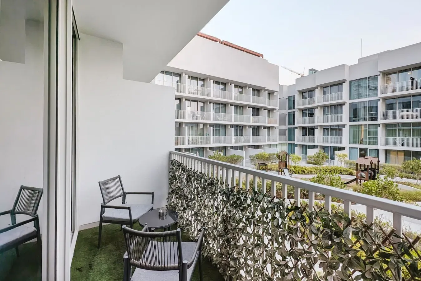 Un balcón con asientos al aire libre da a un patio ajardinado y edificios circundantes.