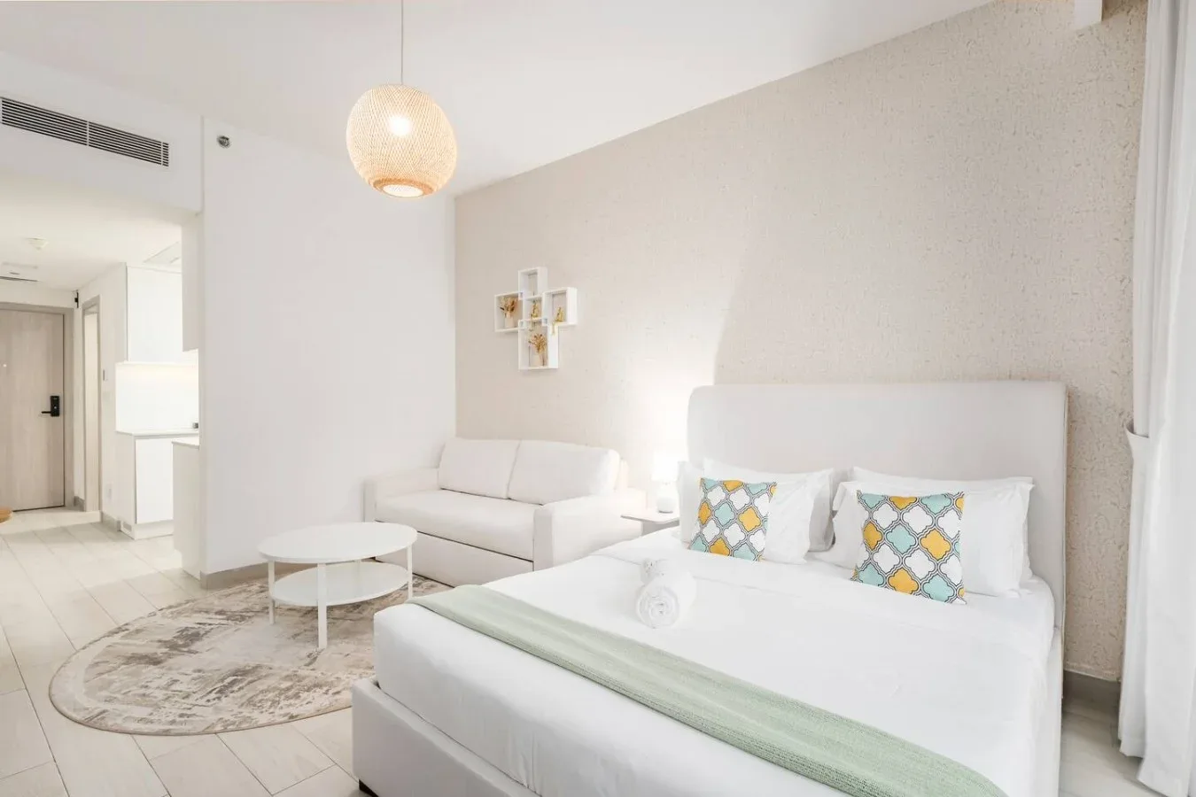 Un dormitorio luminoso con una cama, una pequeña zona de estar y una mesa de centro redonda.