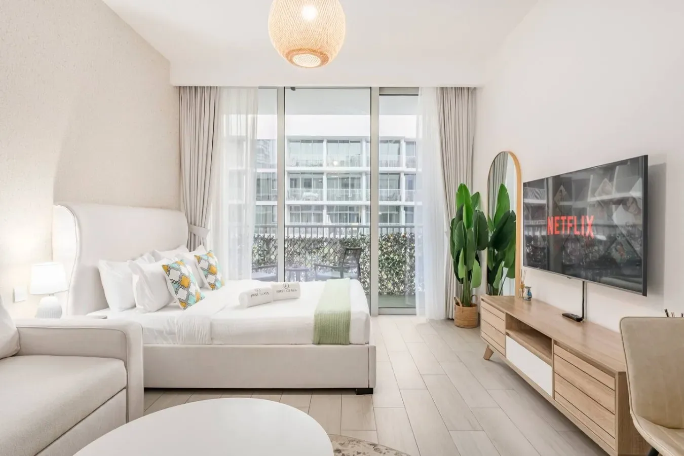 Un dormitorio luminoso con una cama frente a un televisor montado en la pared y grandes ventanas.