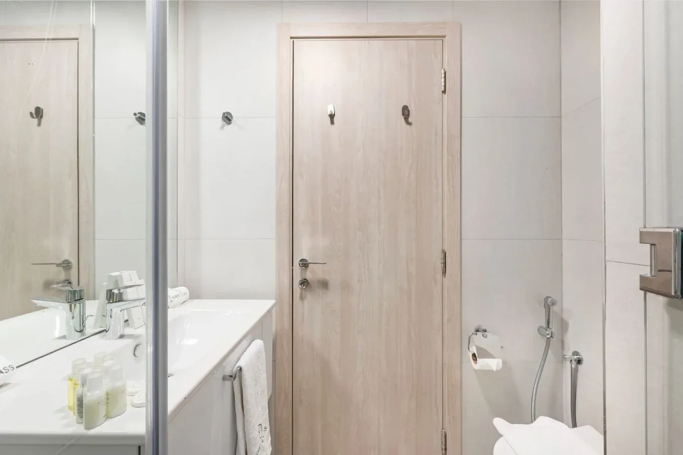Un baño alicatado con una puerta color madera, lavabo y accesorios de pared.