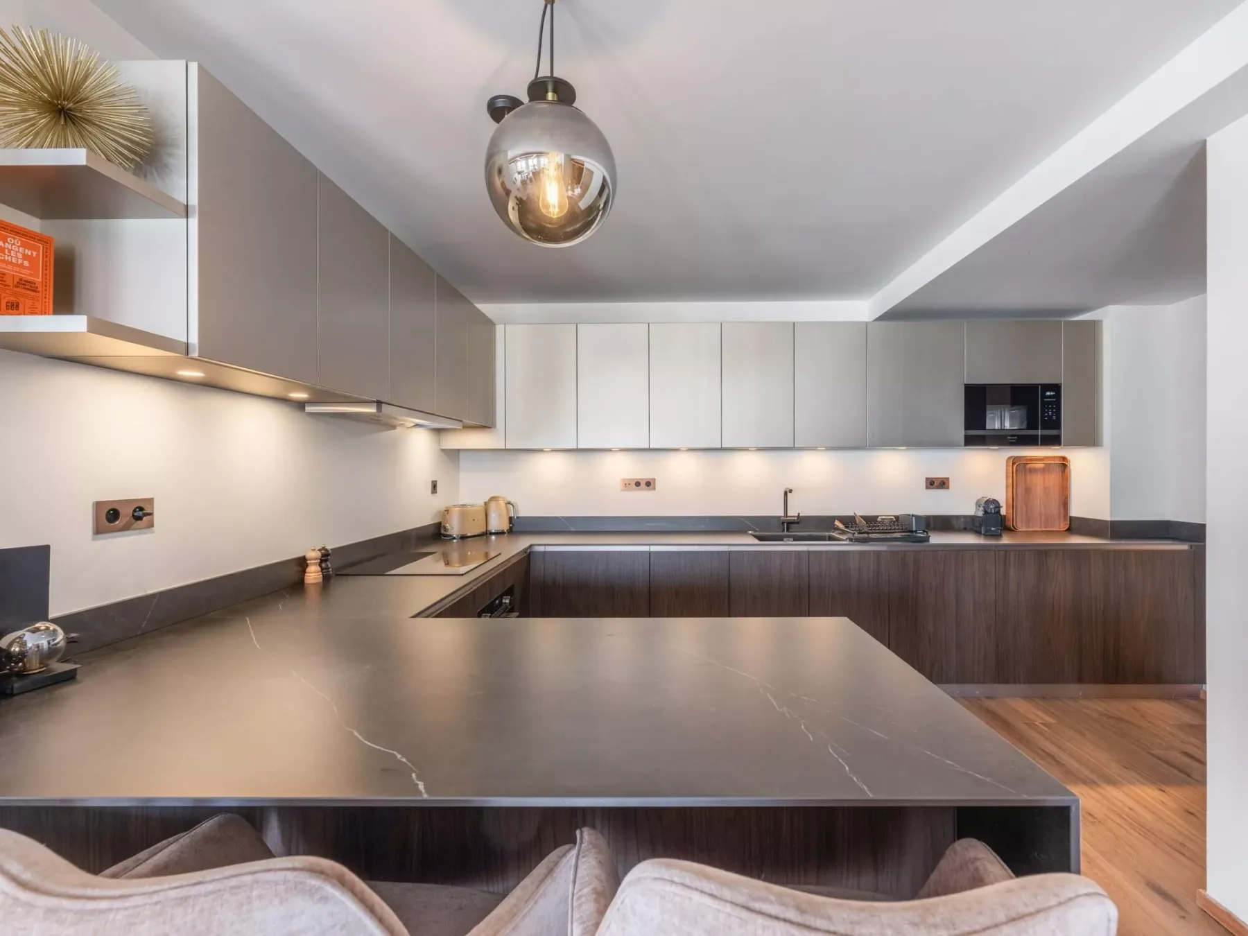 A modern kitchen with gray cabinetry, dark countertops, and a large central island.