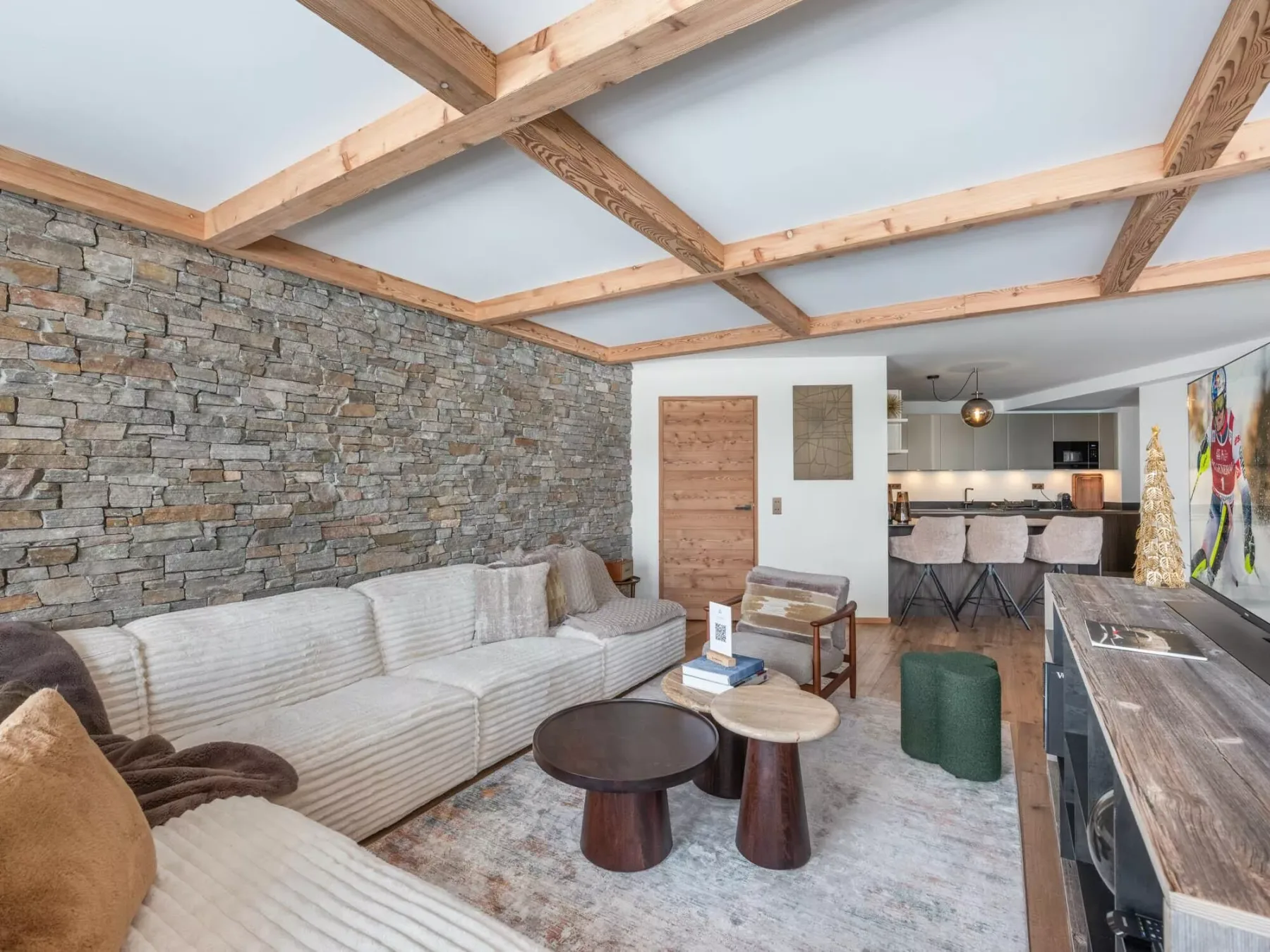 Una sala de estar con asientos junto a una pared de piedra y una cocina abierta.