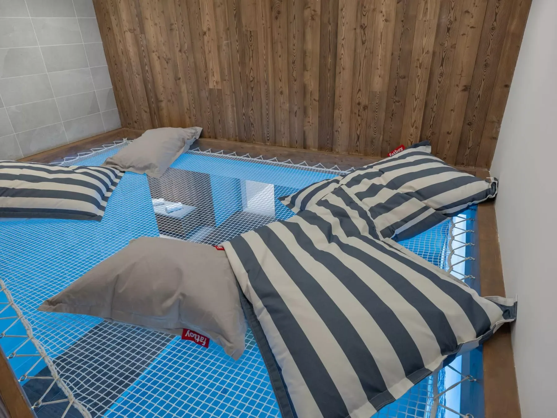 Una zona para dormir con red, ropa de cama a rayas y almohadas junto a una pared de madera.