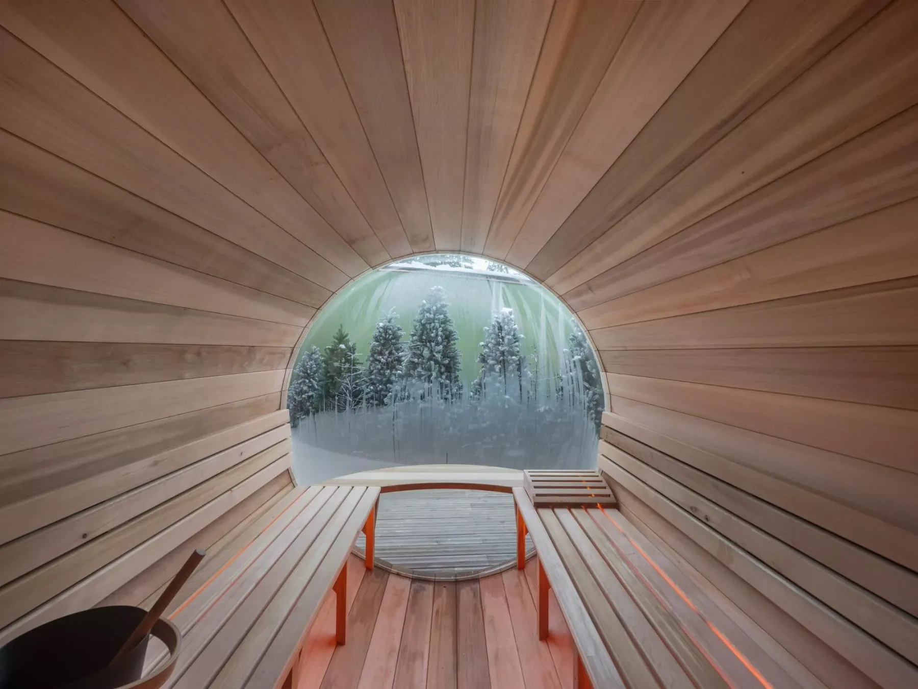 Una sauna revestida de madera tiene bancos frente a una gran ventana con árboles.