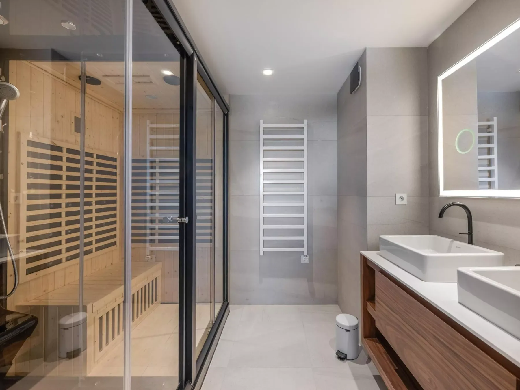 Un baño moderno con una ducha acristalada, un toallero calefactor y un tocador.
