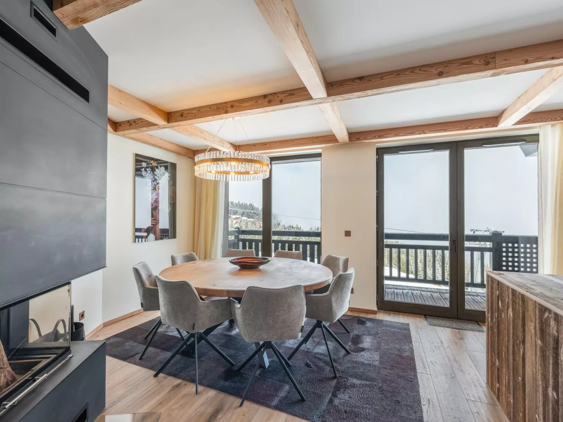 A dining area with a round table and large windows opening onto a balcony.