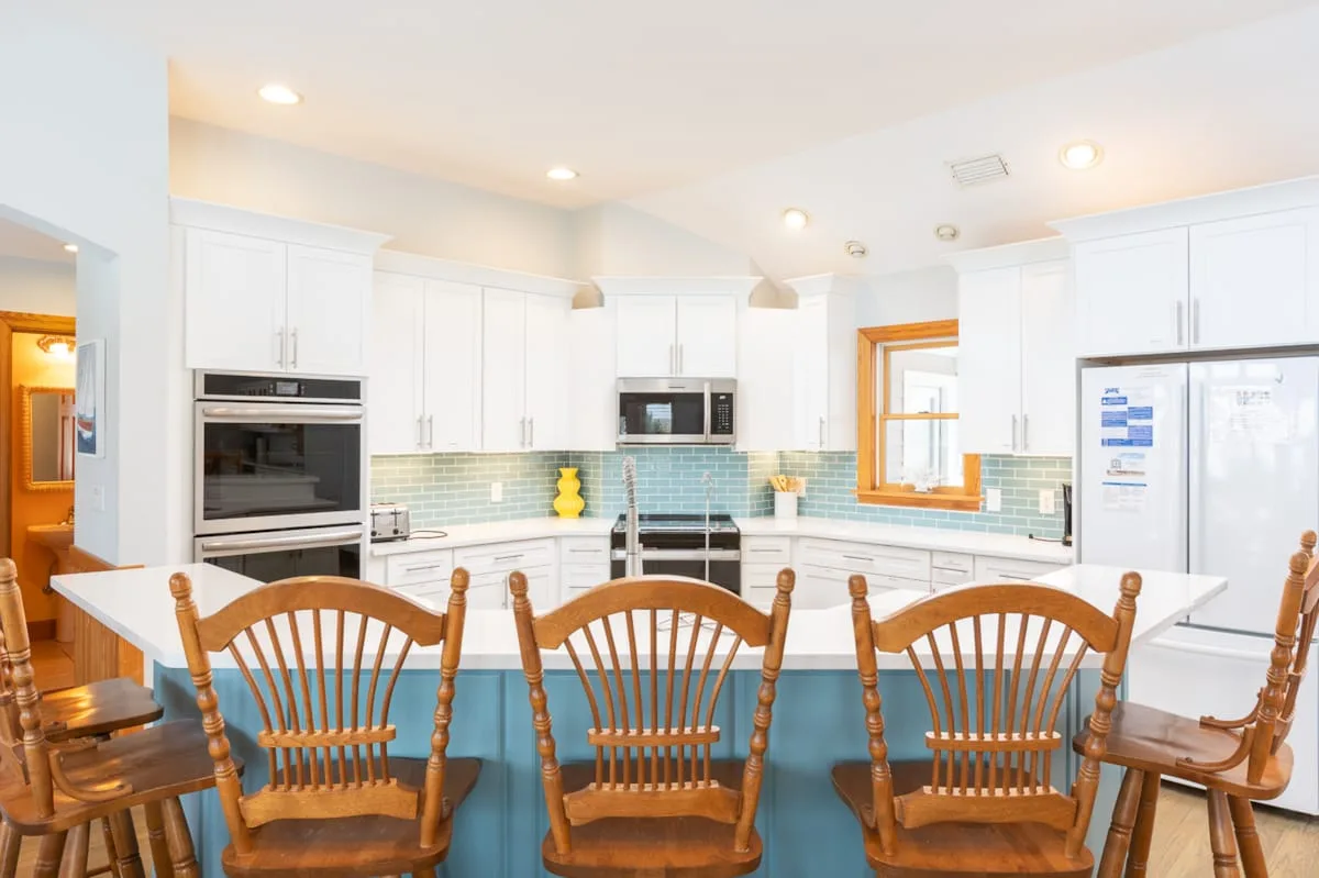 Una cocina luminosa con gabinetes blancos, un salpicadero de azulejos y una isla amplia.
