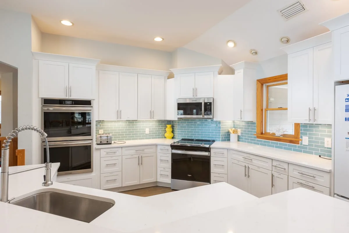 Una cocina luminosa con gabinetes blancos, electrodomésticos de acero inoxidable y un salpicadero de azulejos.