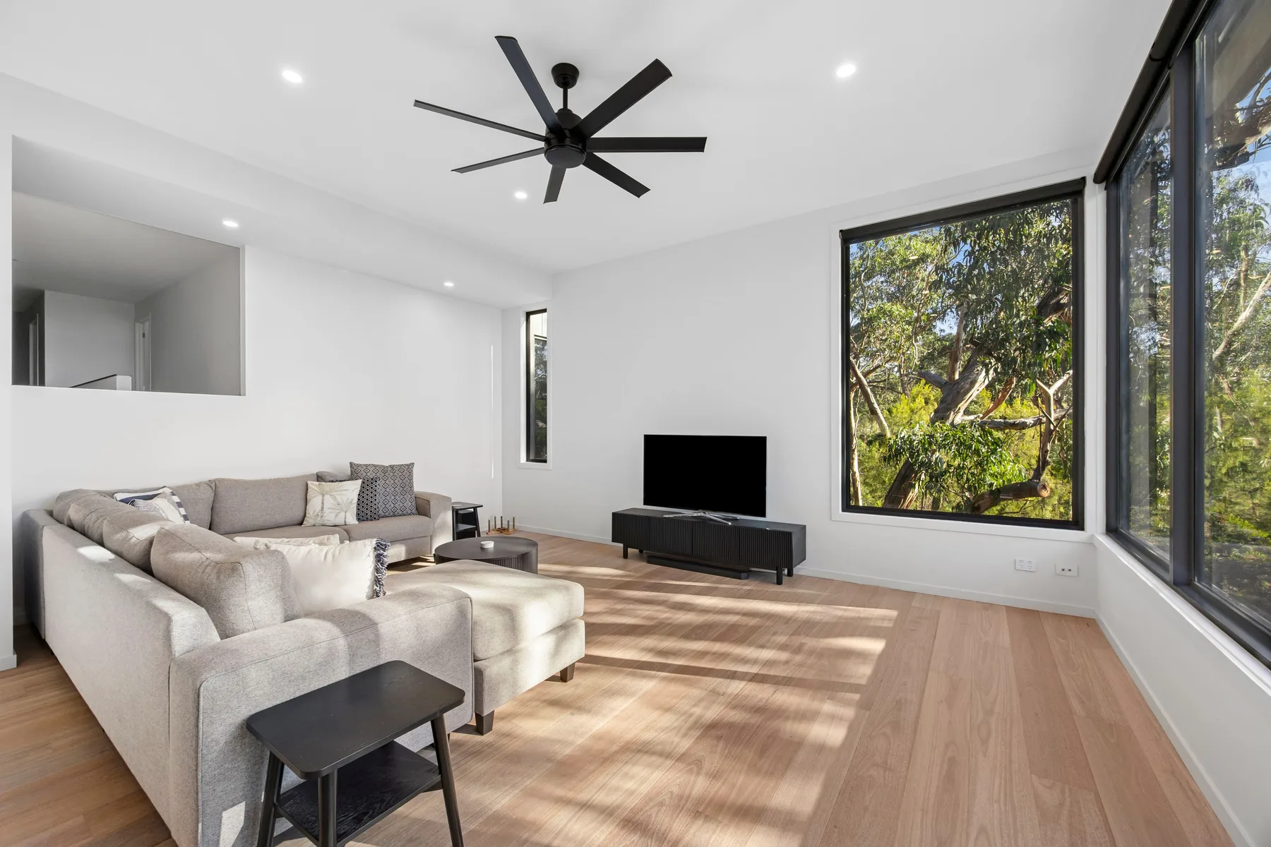 Una sala luminosa con asientos, un televisor y grandes ventanas con vistas a los árboles.