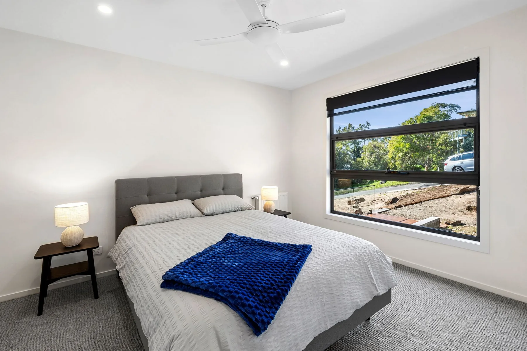 Un dormitorio luminoso con una cama junto a una gran ventana con vistas a la vegetación.