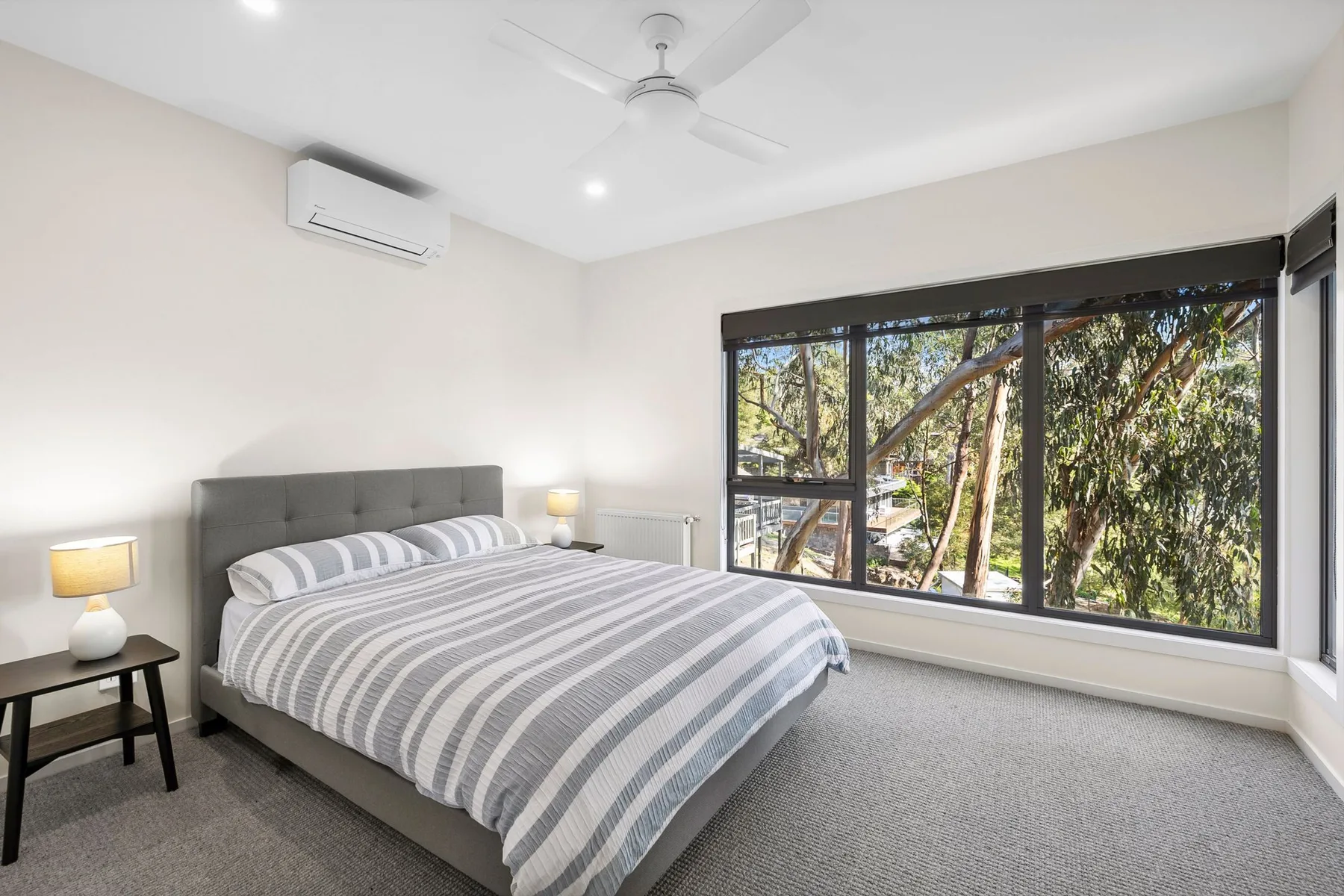 Un dormitorio luminoso con una cama junto a una gran ventana con vistas a los árboles.