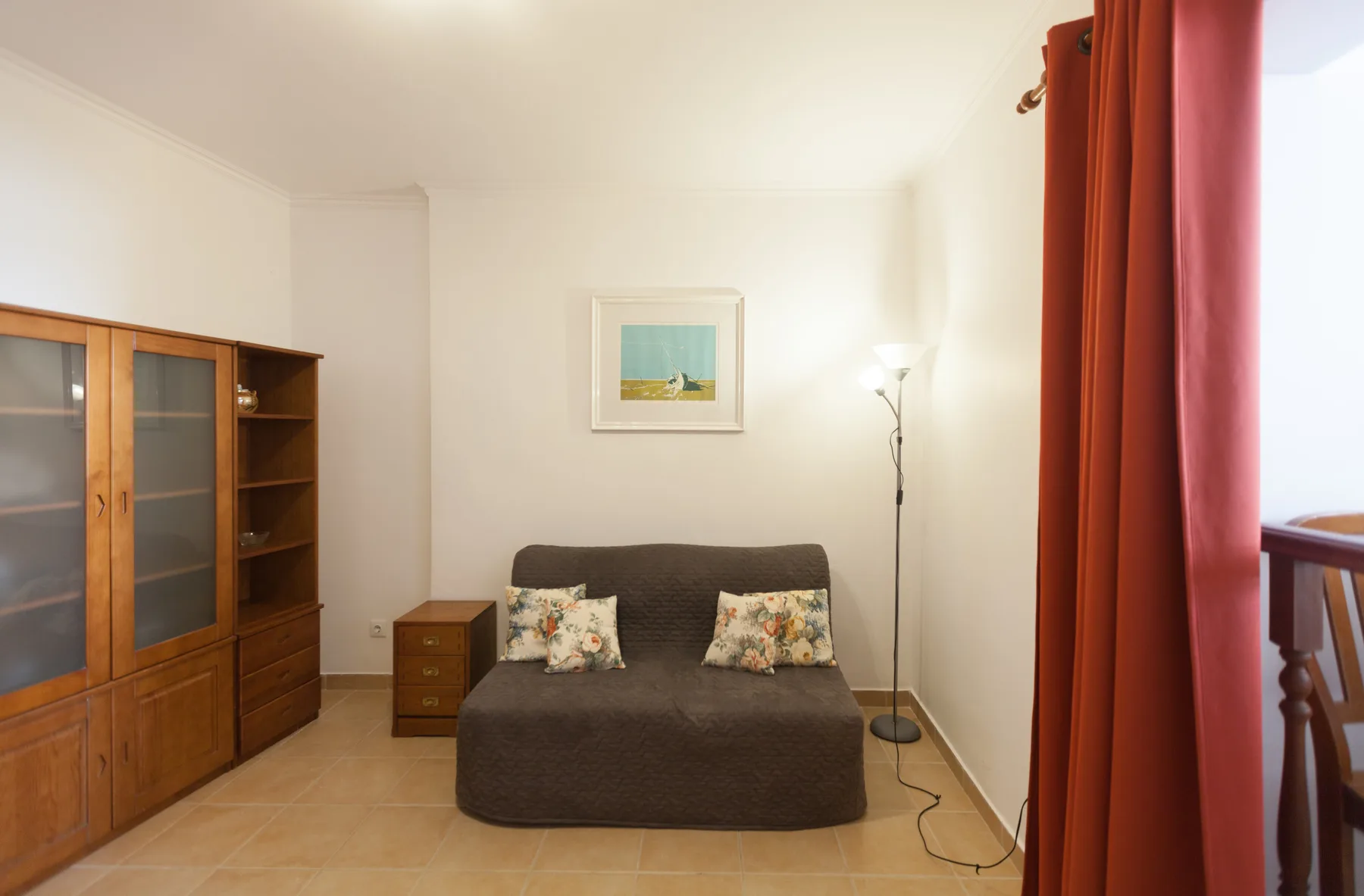 Una sala de estar con un sofá oscuro, un mueble de madera y cortinas rojas.