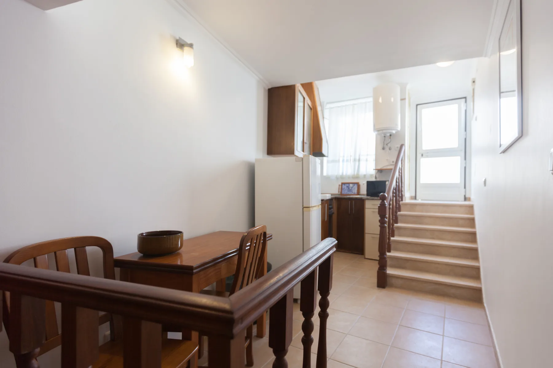 A dining area with wooden seating sits beside a staircase and small kitchen.