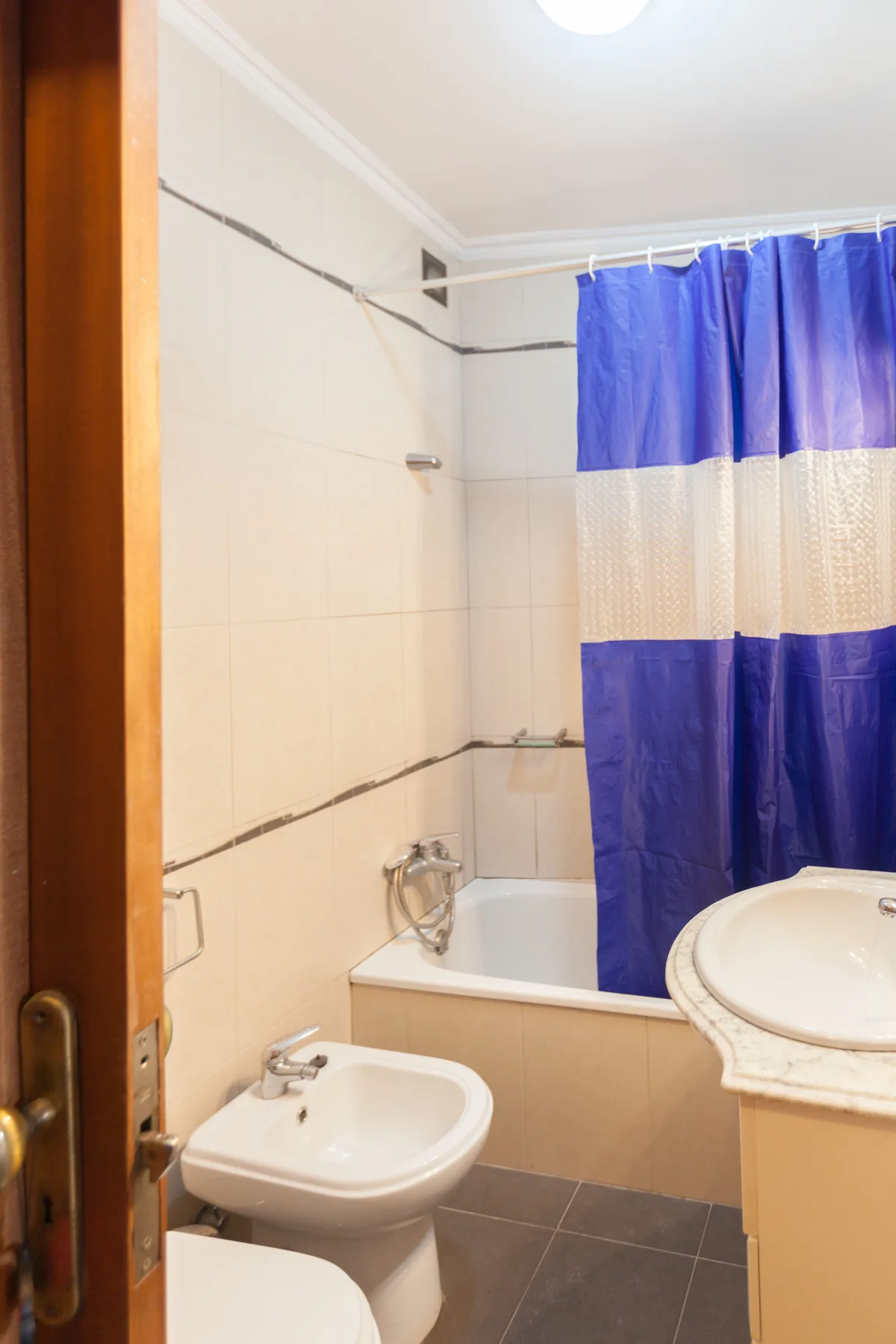 Un baño alicatado con bañera, lavabo y cortina de ducha azul.