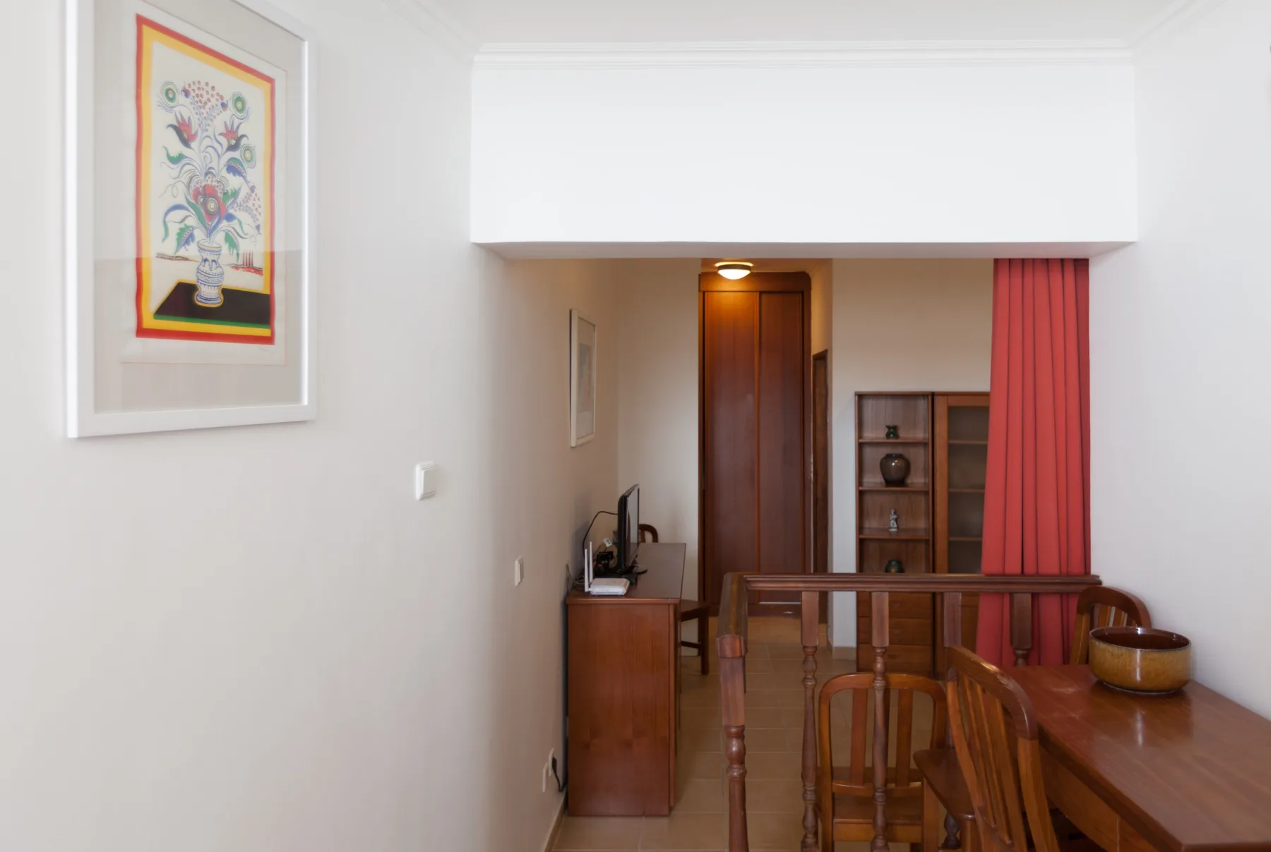 A dining area with wooden furniture, framed artwork, and a red curtain.