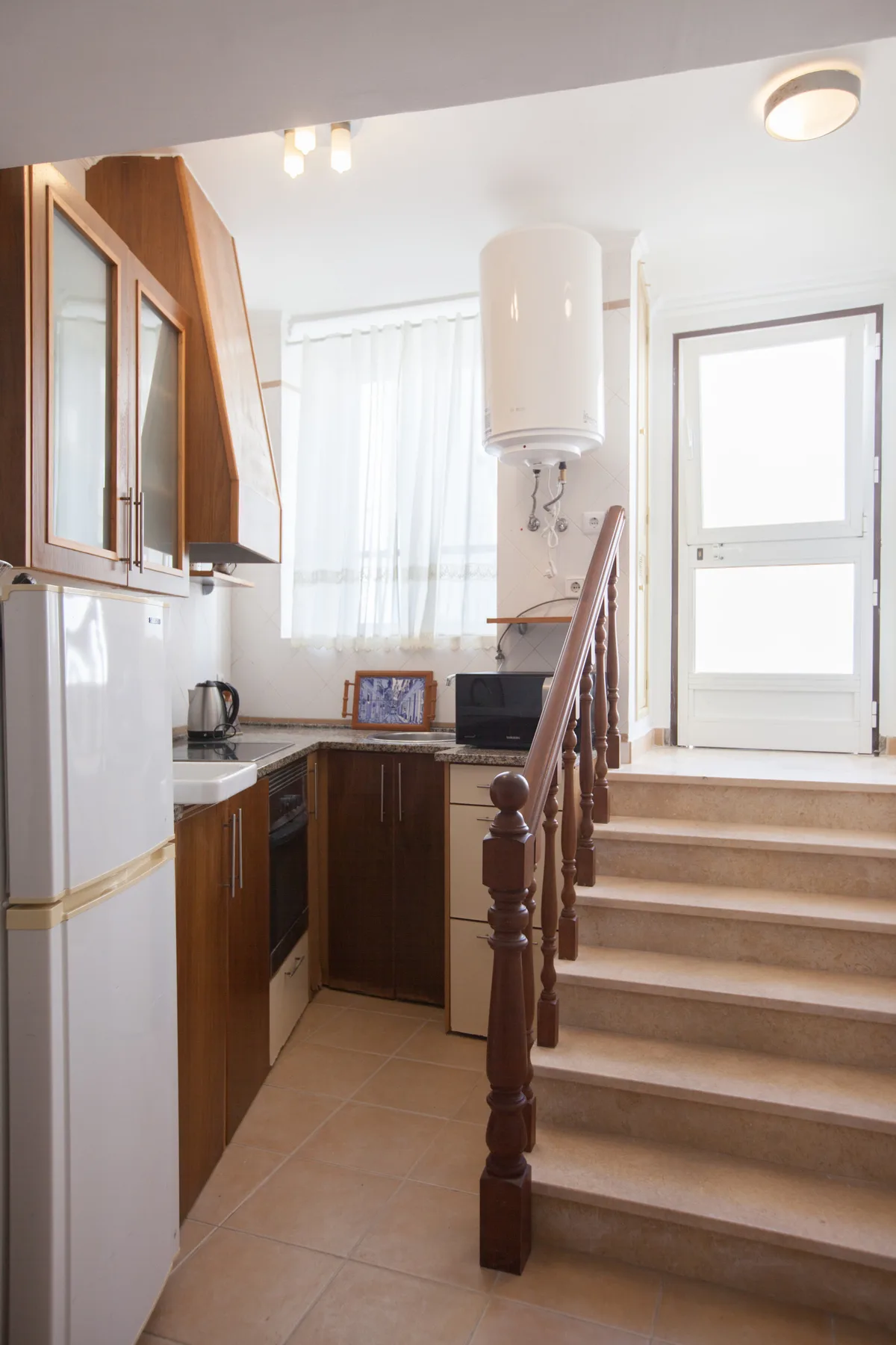 Una cocina compacta junto a una escalera que conduce a una puerta luminosa.