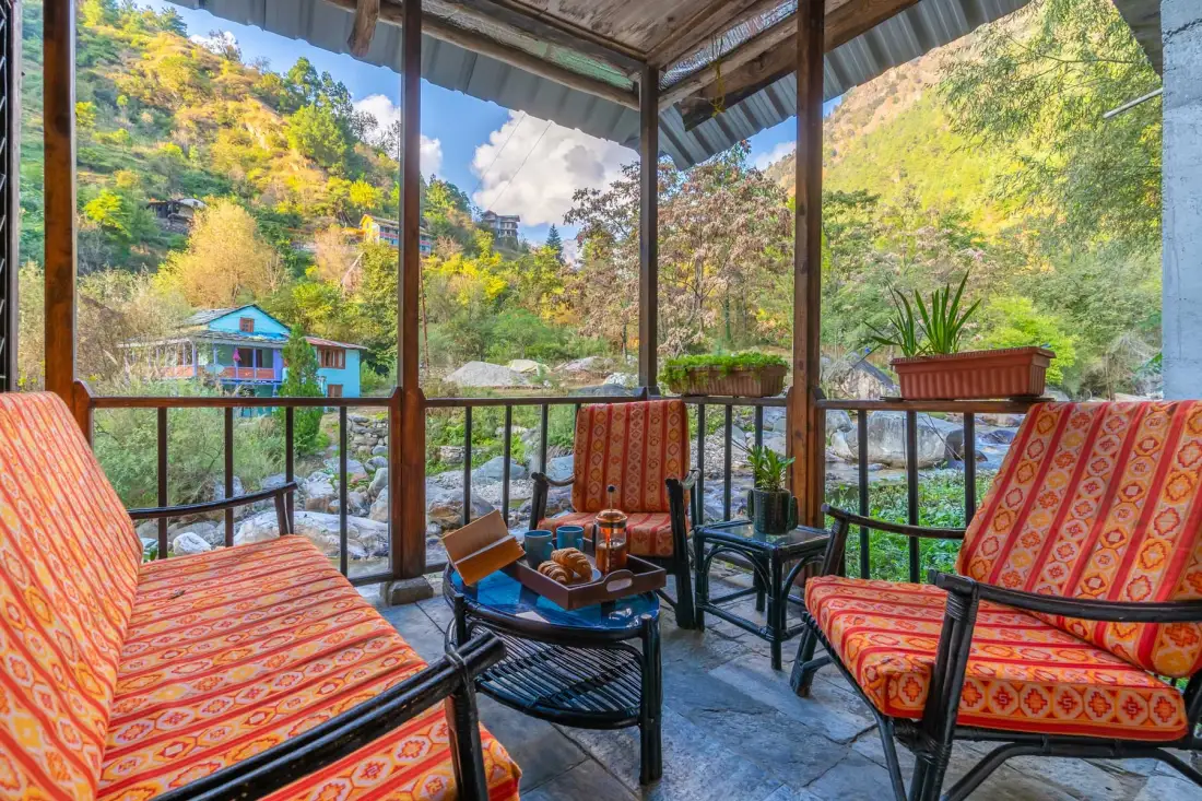 A covered outdoor seating area overlooks a rocky stream and green hills.