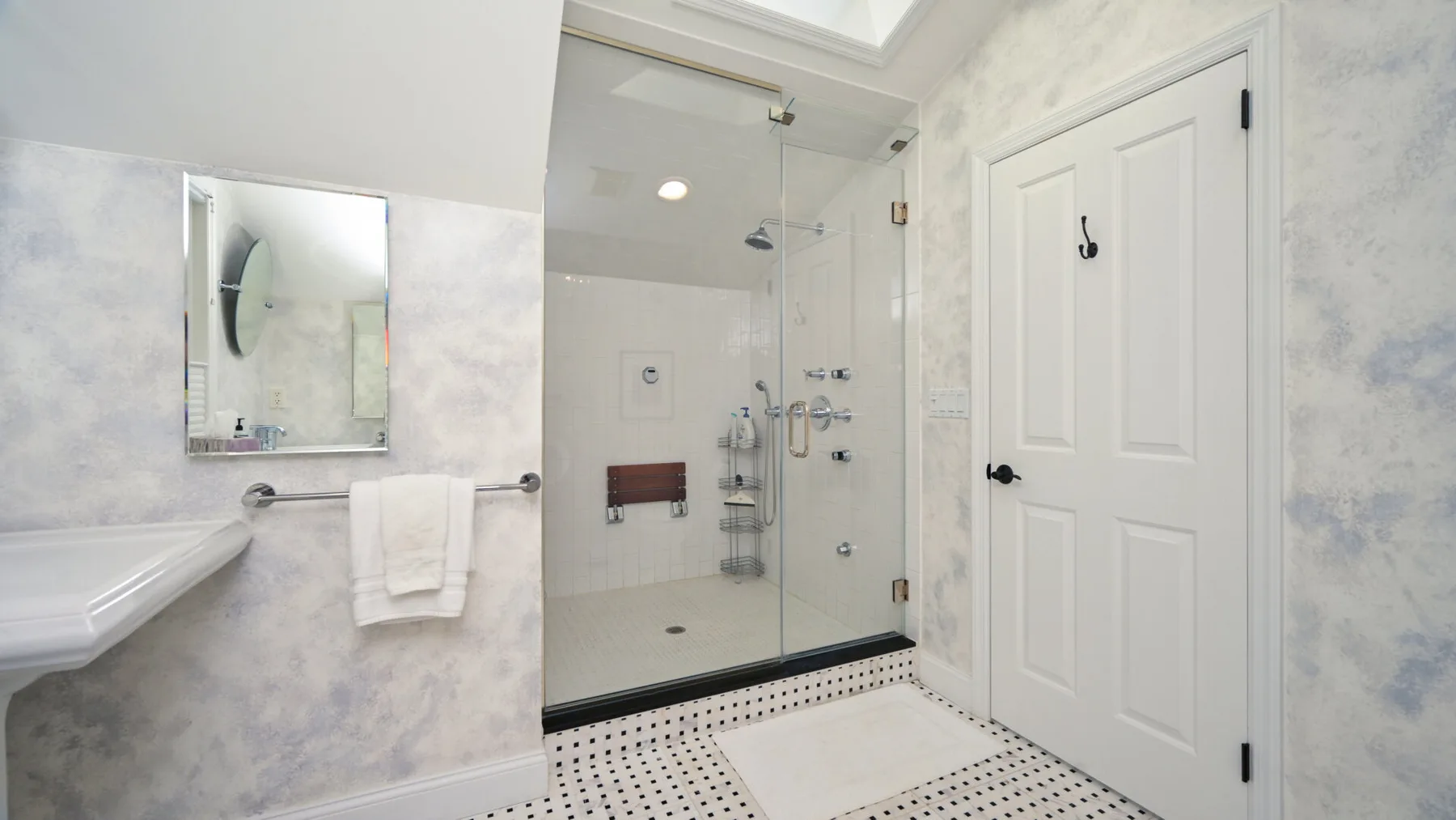 Un baño con azulejos, ducha de vidrio, lavabo y puerta blanca.