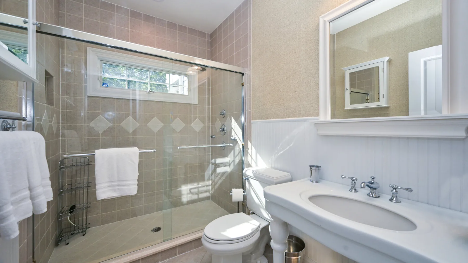 Un baño alicatado tiene una ducha de vidrio, un inodoro y un lavabo amplio.