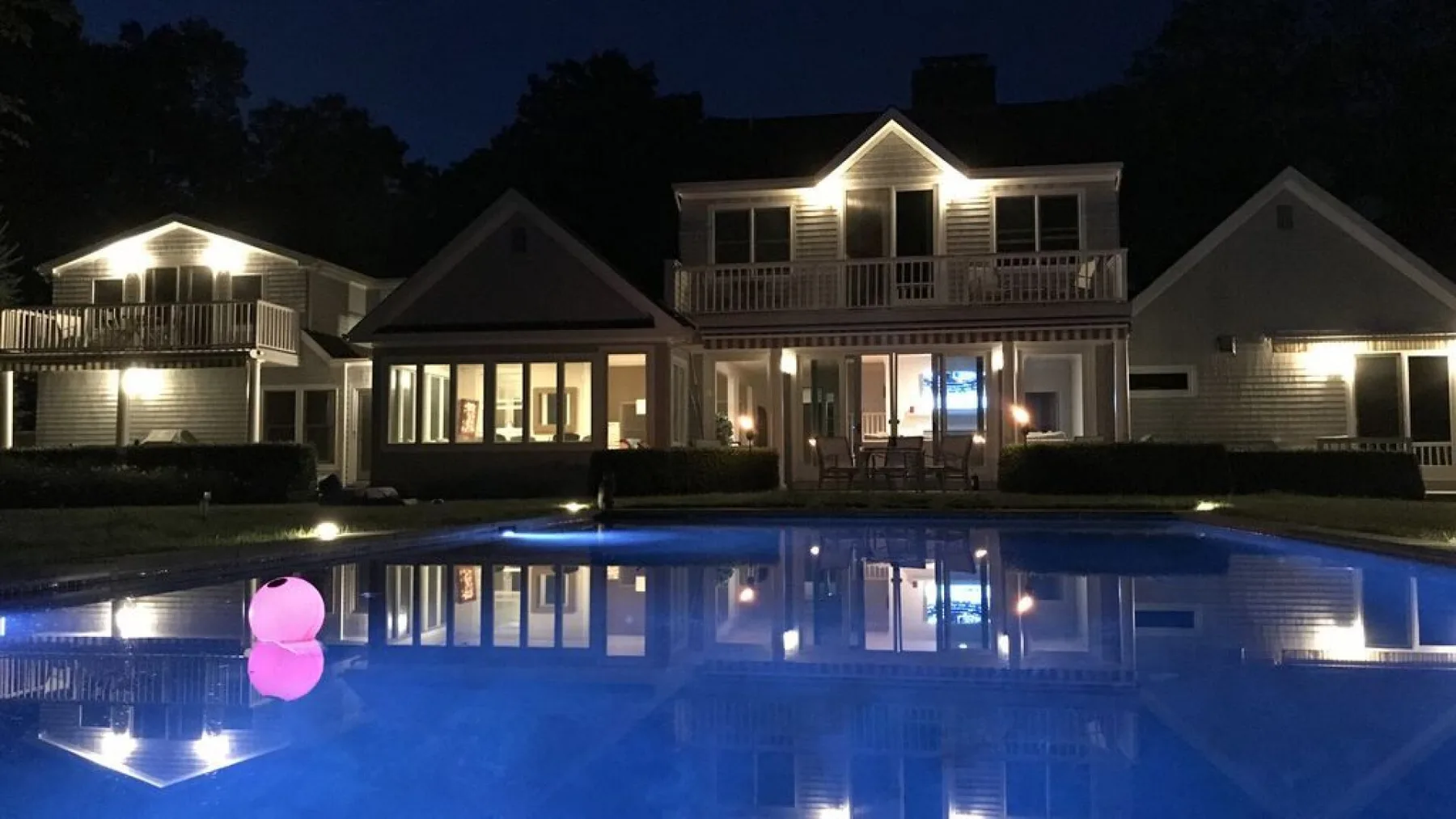 Una piscina refleja una casa bien iluminada por la noche.