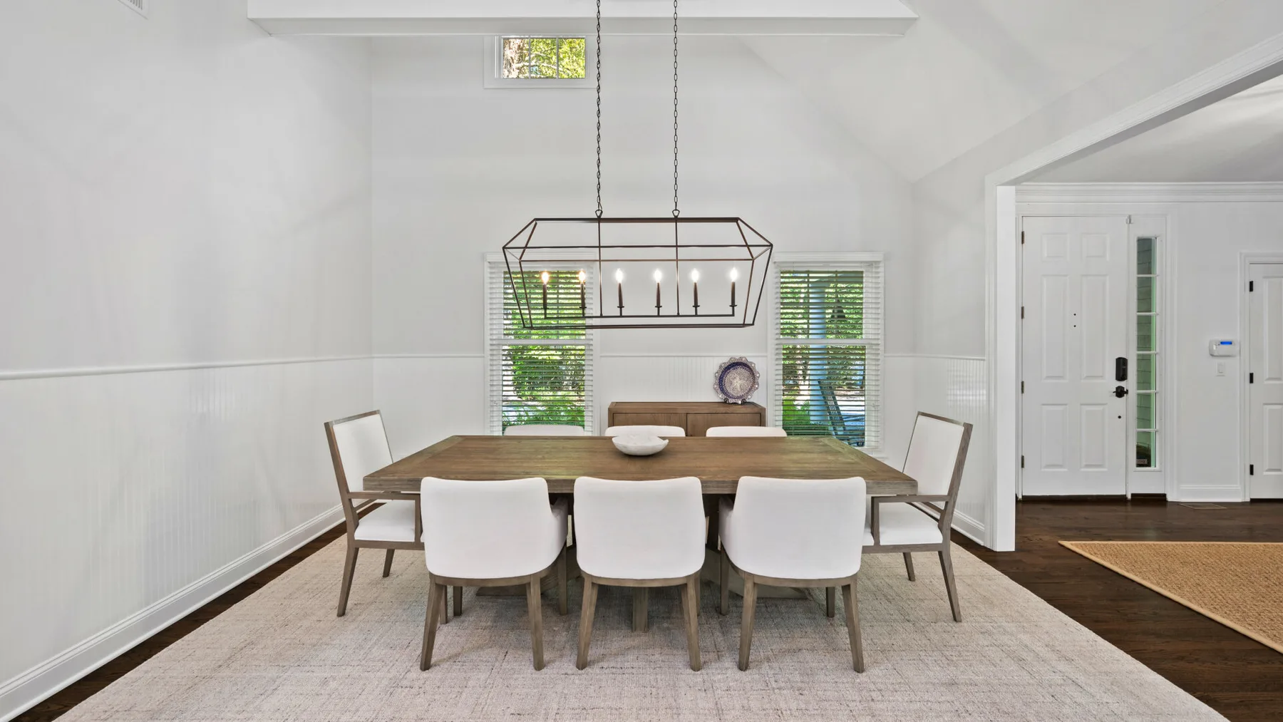 Un comedor luminoso con una mesa larga bajo una lámpara colgante.