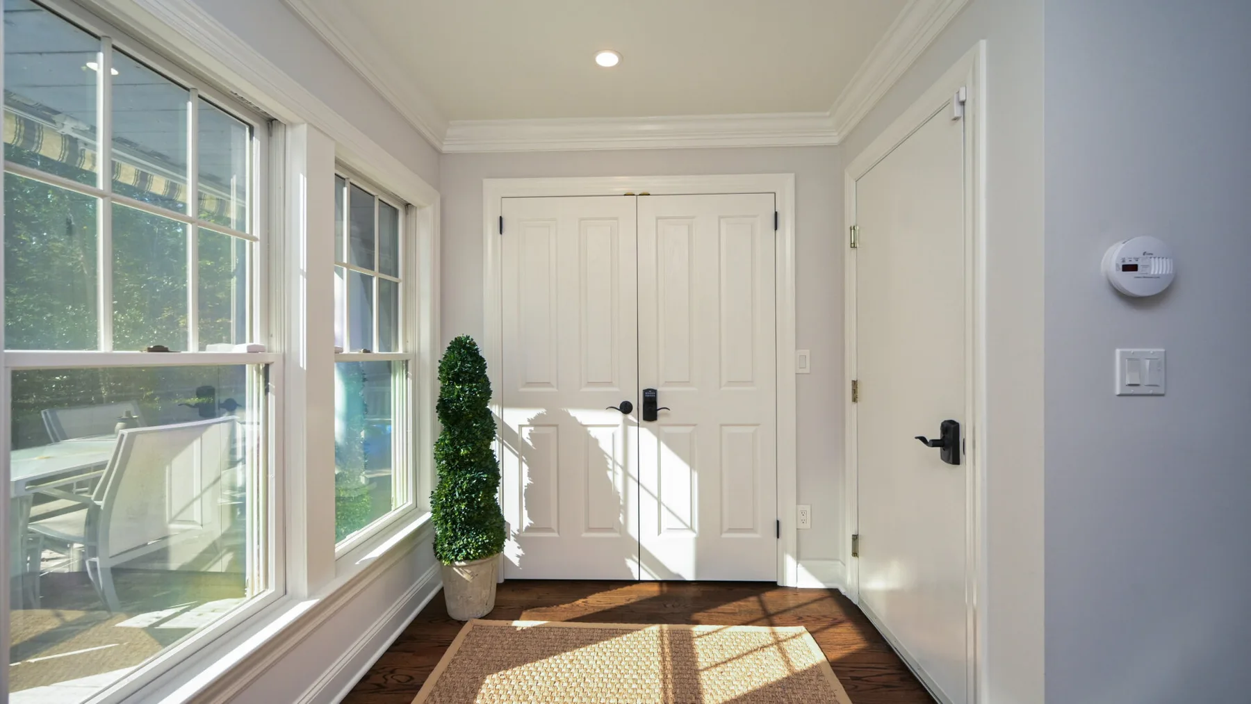Una entrada luminosa con puertas blancas y grandes ventanas con vistas a la vegetación.