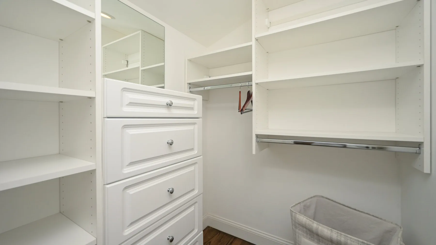Un vestidor con estantes blancos, cajones y una barra para colgar ropa.