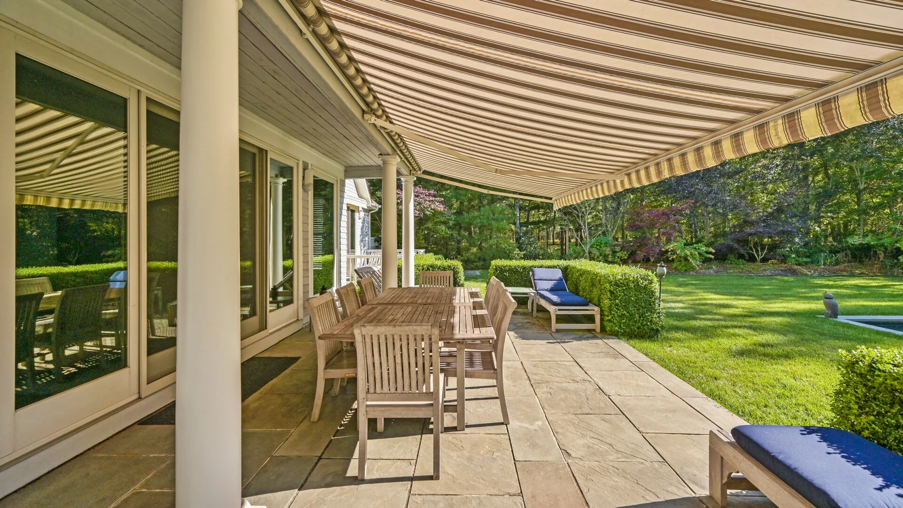 Un patio exterior cubierto con una mesa de comedor y asientos junto a un césped verde.