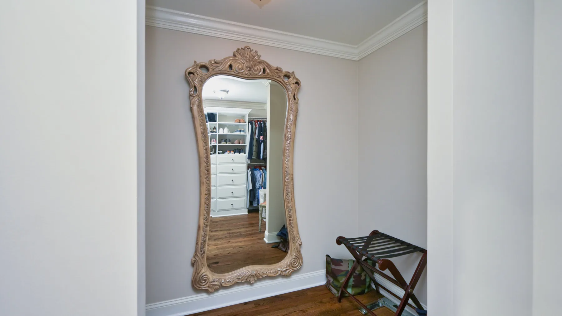 Un espejo decorativo refleja una zona de ropa en un pequeño vestidor.