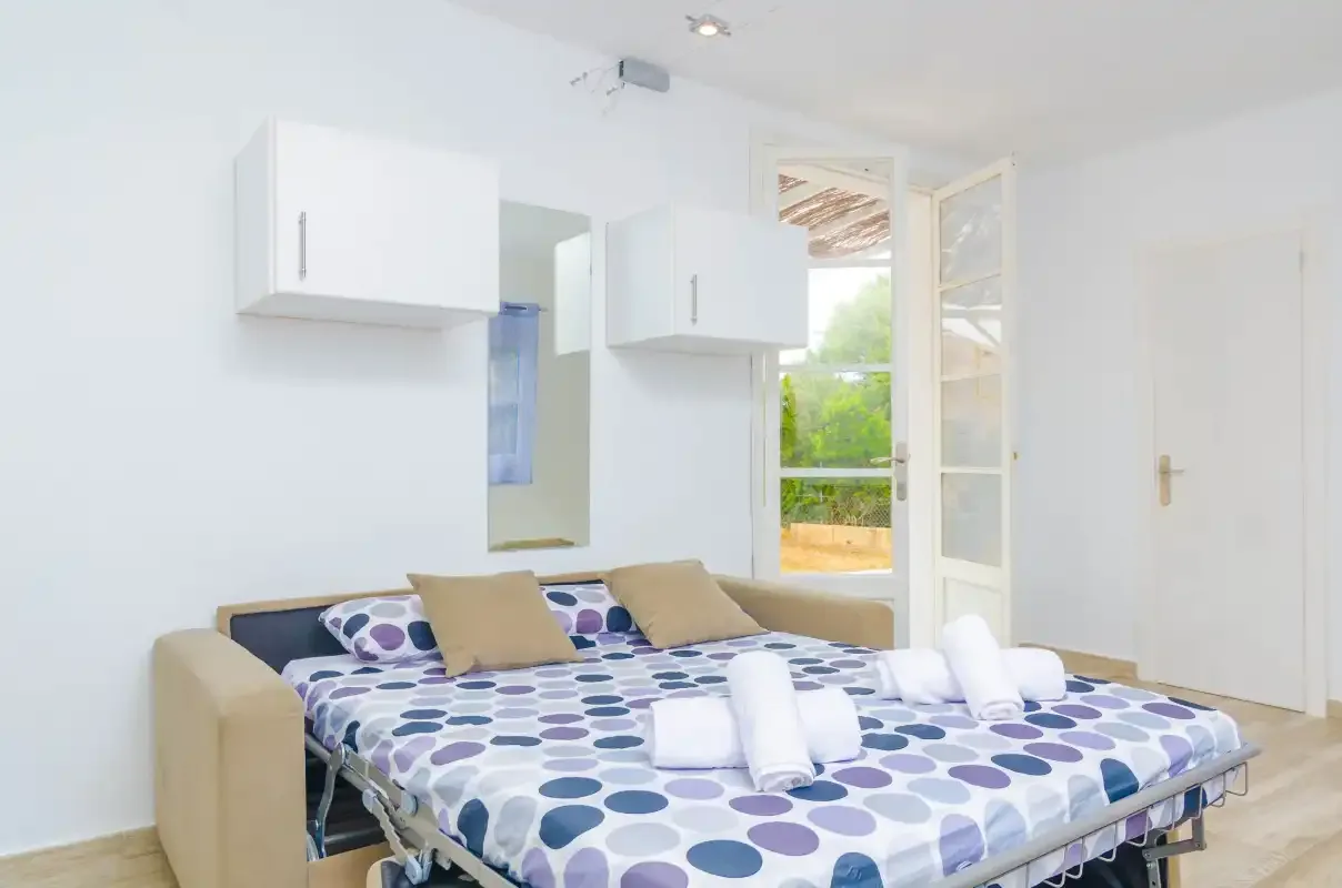 A bright bedroom with a double bed and patterned bedding beside open windows.