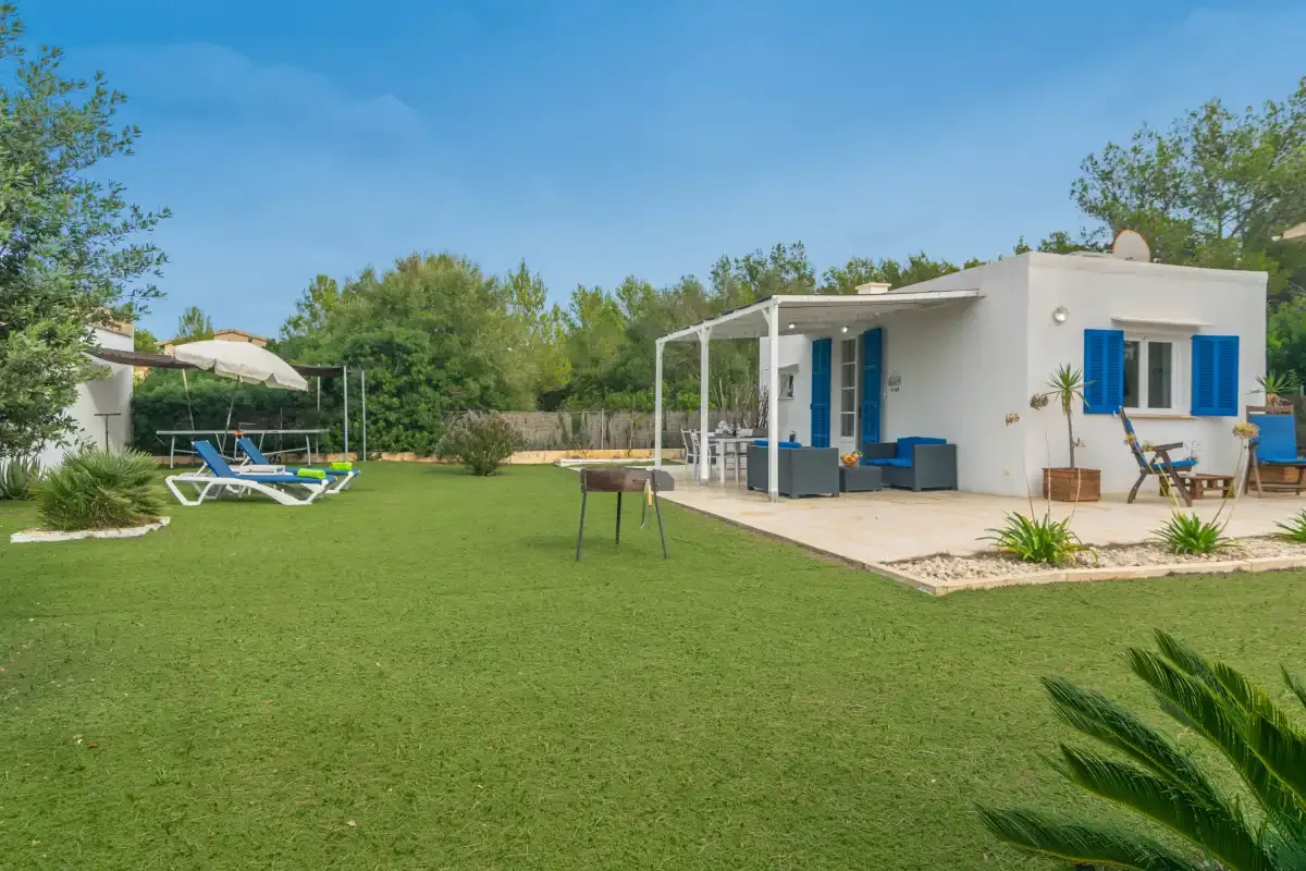 A white house with a covered patio overlooks a broad lawn and outdoor seating.