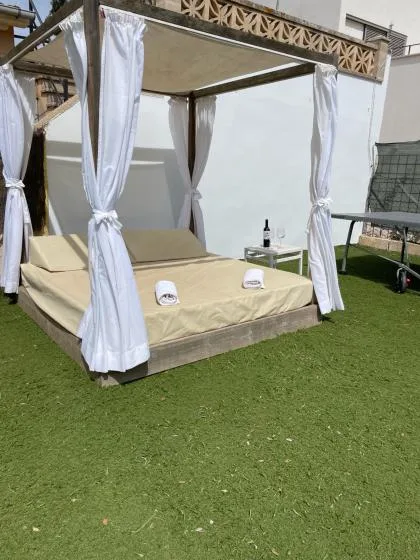 An outdoor covered daybed with white curtains sits on a green lawn.