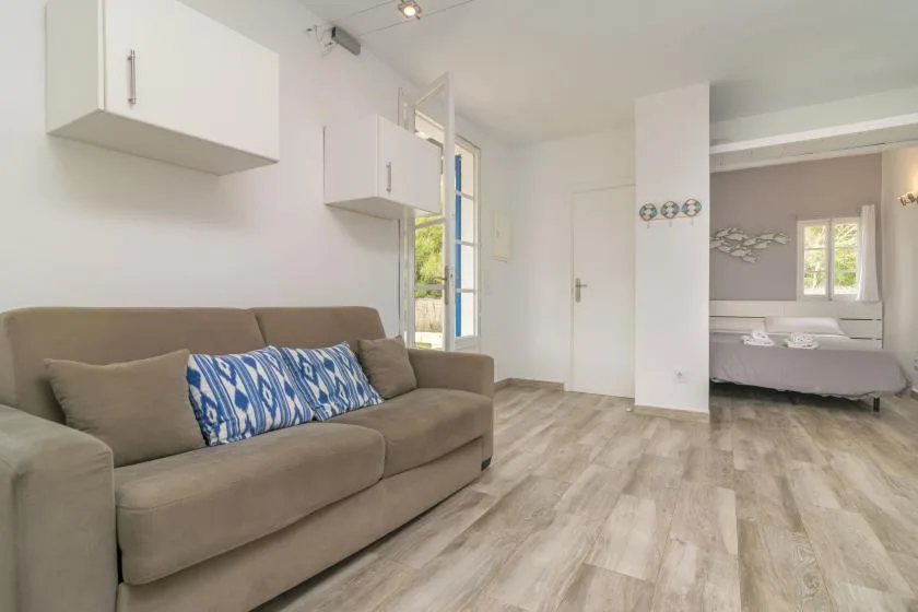 A bright living area with a sofa and an open view of a bed in the adjoining space.