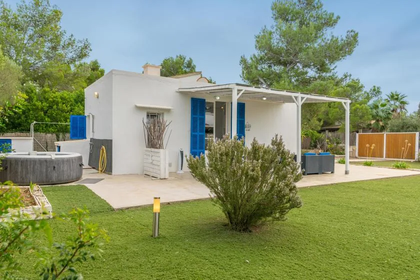 A white house with a covered patio opens onto a green lawn.