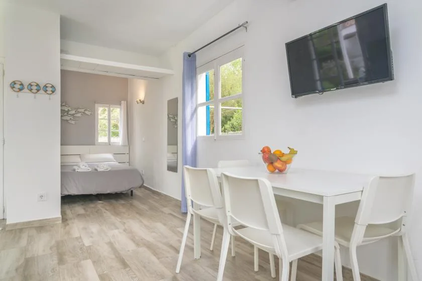 A bright room combines a white dining table with a bed in the adjoining area.