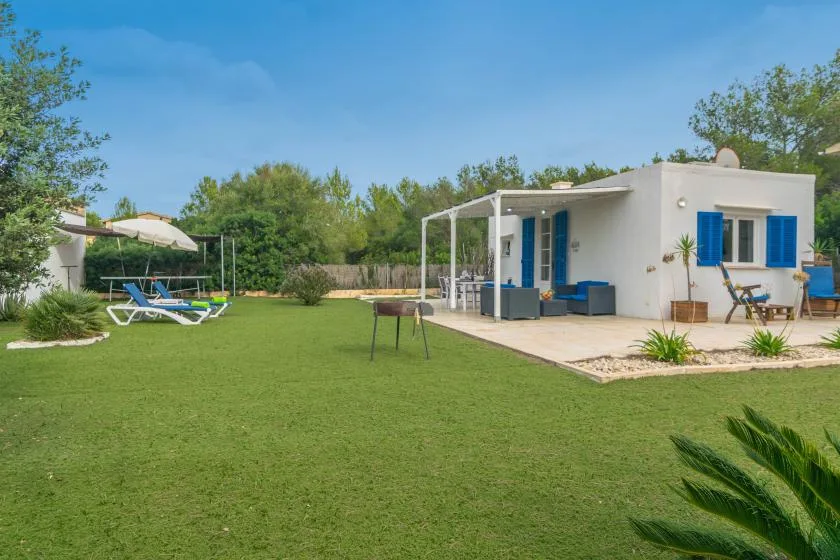 A white house opens onto a broad lawn with outdoor seating and a shaded patio.