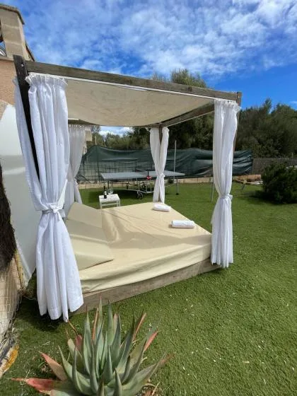 A curtained outdoor cabana with a cream-colored daybed sits on a grassy lawn.