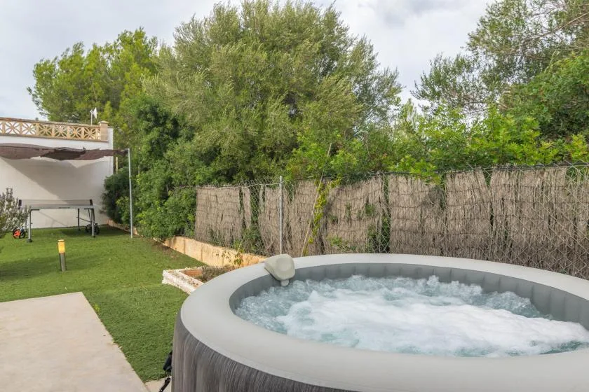 An outdoor hot tub sits beside a grassy yard and leafy trees.