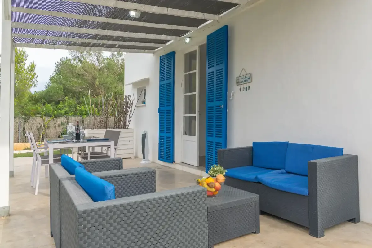 A covered patio with outdoor seating and a dining table overlooks a green garden.