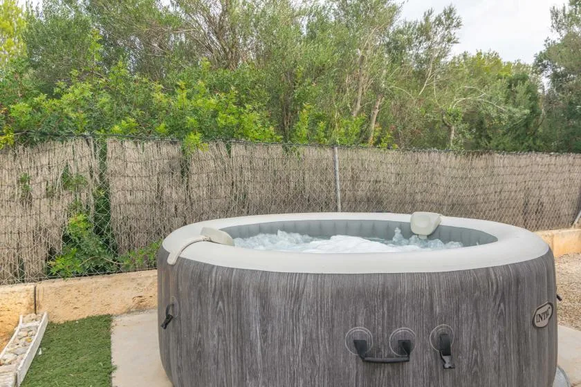 An outdoor hot tub sits beside a reed privacy screen and greenery.