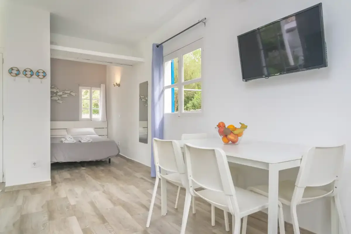 A bright dining area with white seating and a table beside a bedroom.
