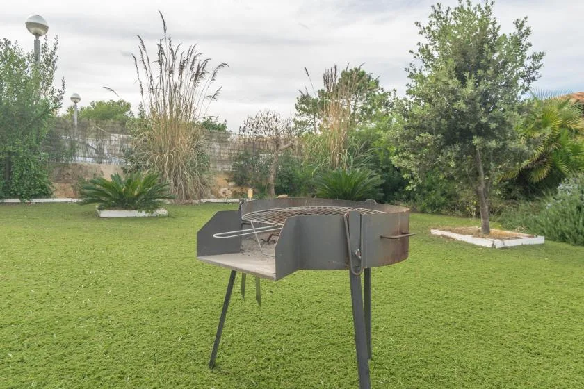 A barbecue grill stands on a grassy lawn surrounded by trees and plants.