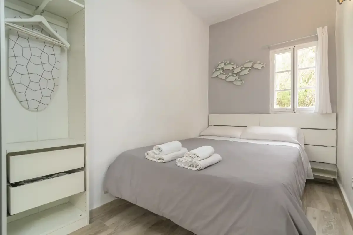 A bedroom with a neatly made bed and a window overlooking greenery.