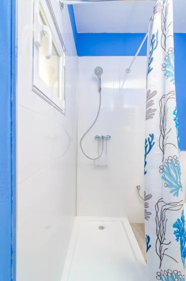 A bright tiled shower area with a handheld showerhead and patterned curtain.