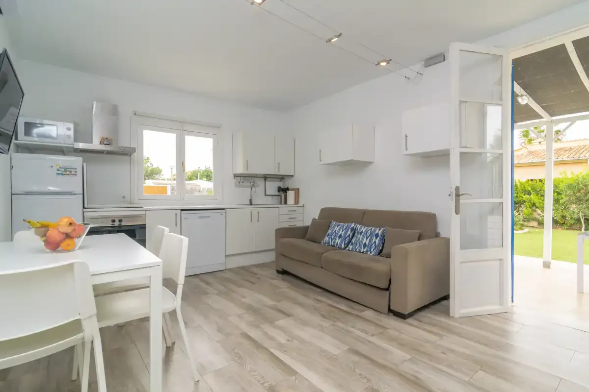 A bright open-plan kitchen and living area with a dining table and sofa.