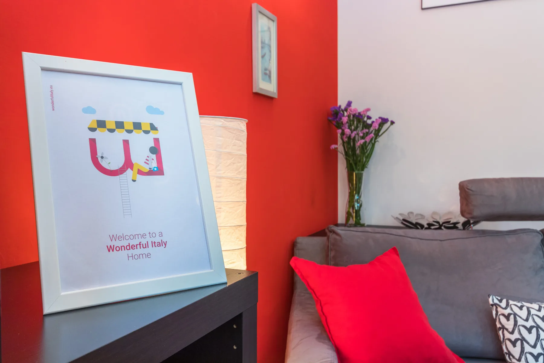 Una sala de estar con asientos grises, un cojín rojo y arte enmarcado en la pared.
